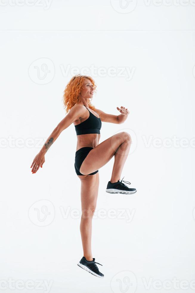 Having exercise. Redhead female bodybuilder is in the studio on white background photo