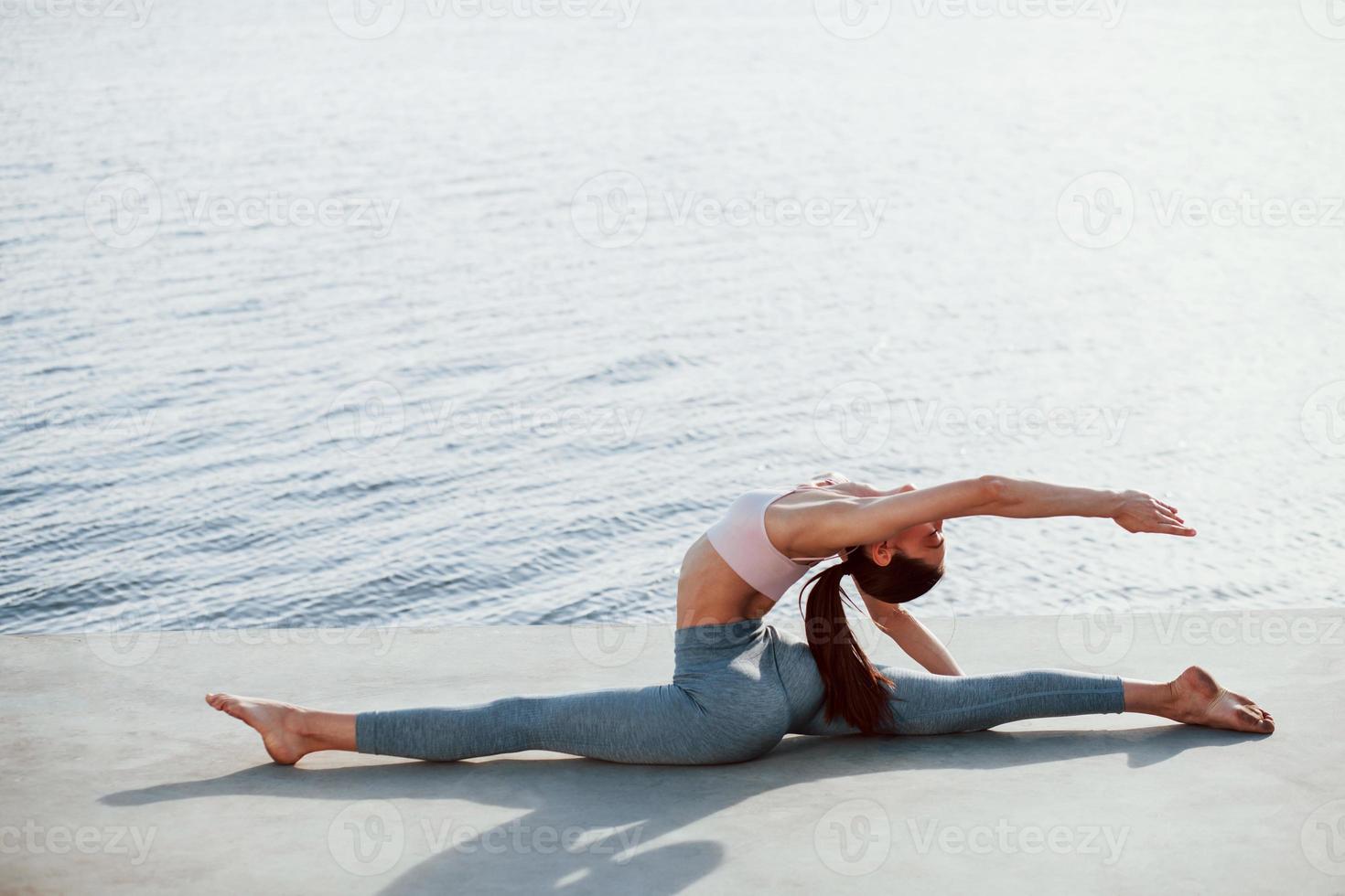 Early morning training. Young woman with slim type of body does exercises against lake photo