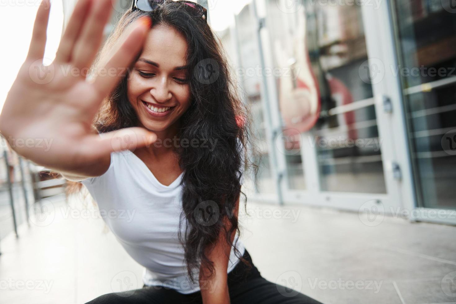 Hands to the camera. Beautiful woman with curly black hair have good time in the city at daytime photo