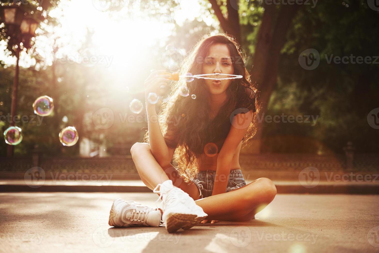 Blowing soap bubble. Beautiful woman with curly black hair have good time in the city at daytime photo