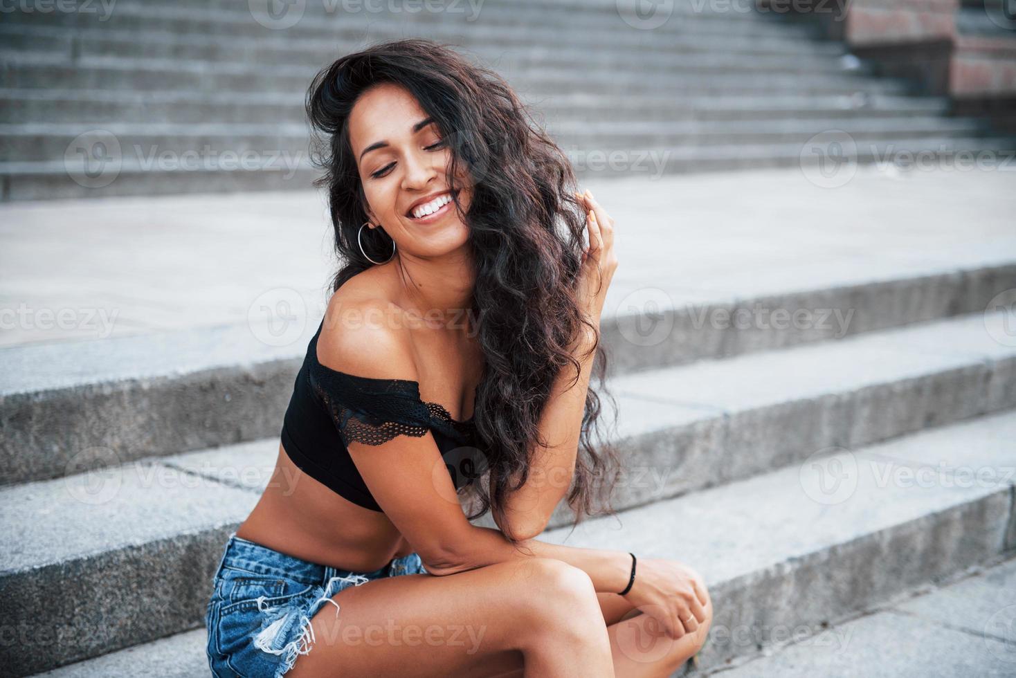 Toothy smile. Beautiful woman with curly black hair have good time in the city at daytime photo