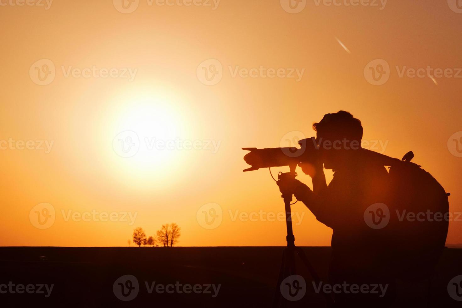 Photographer with professional equipments makes photos. Stands in the field illuminated by sunlight photo