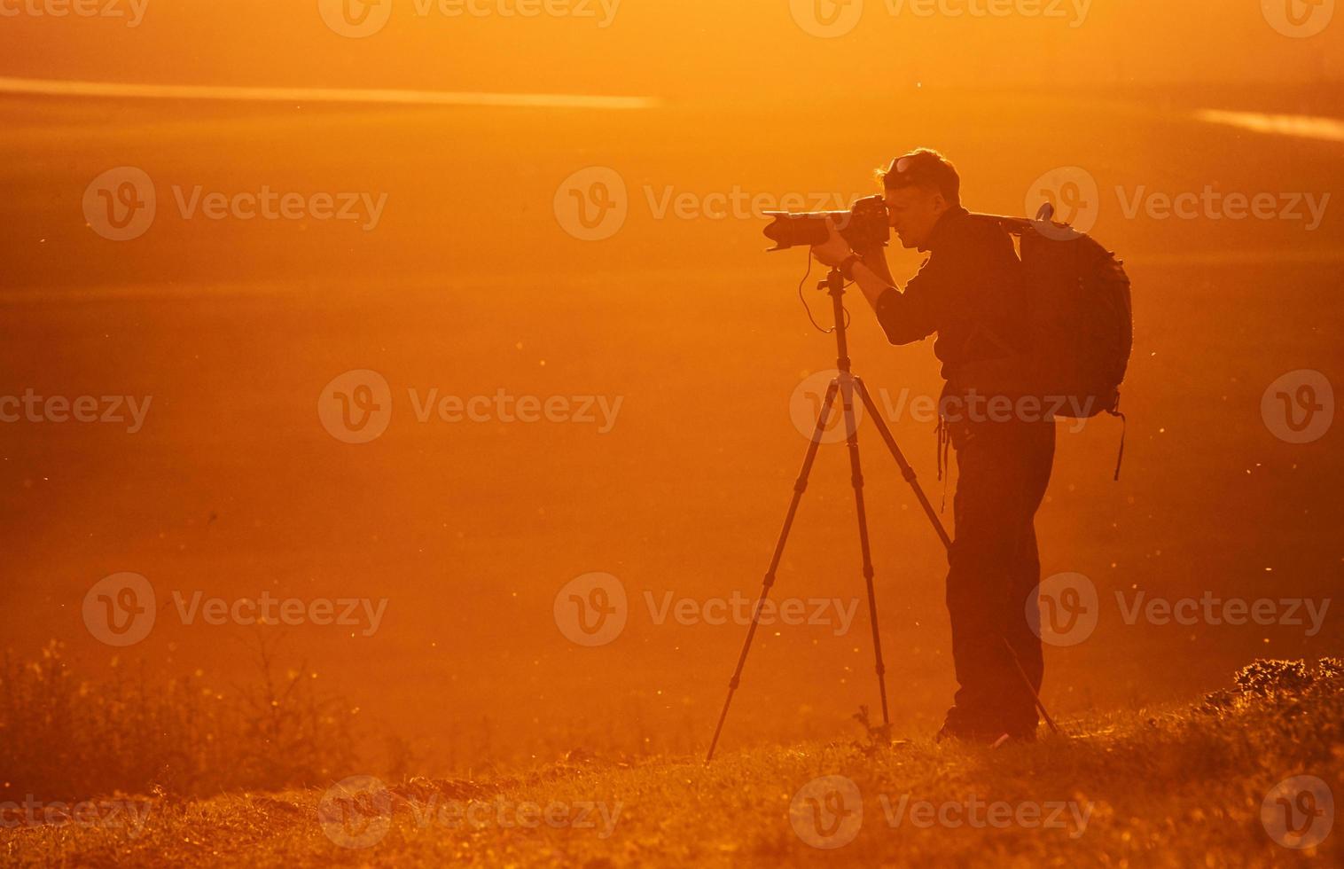 Photographer with professional equipments makes photos. Stands in the field illuminated by sunlight photo