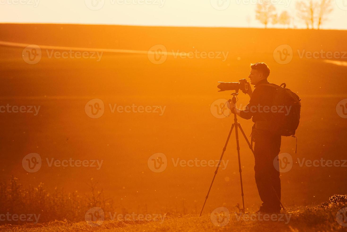 Photographer with professional equipments makes photos. Stands in the field illuminated by sunlight photo
