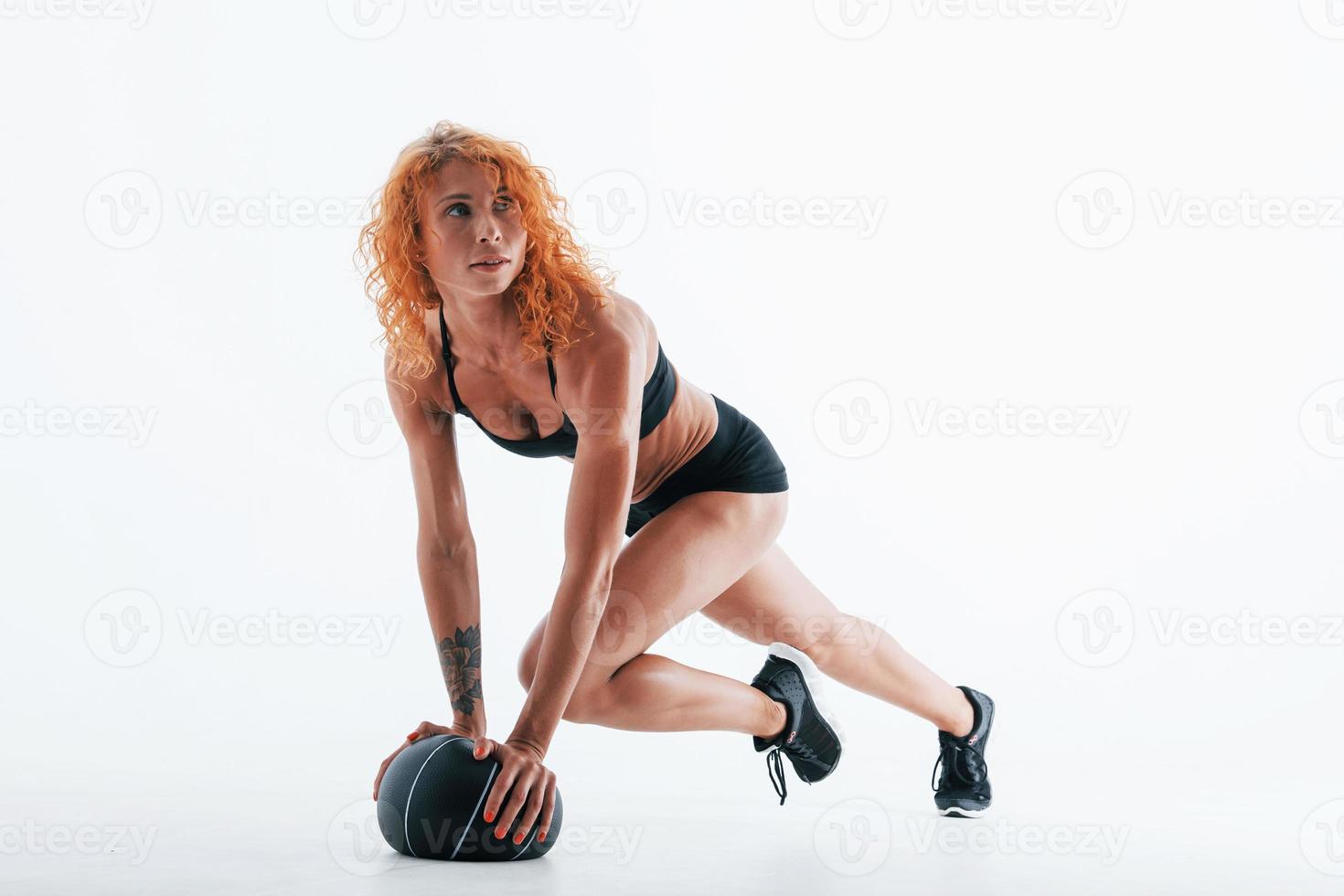 Posing for a camera with soccer ball. Particle view. Redhead female bodybuilder is in the studio on white background photo