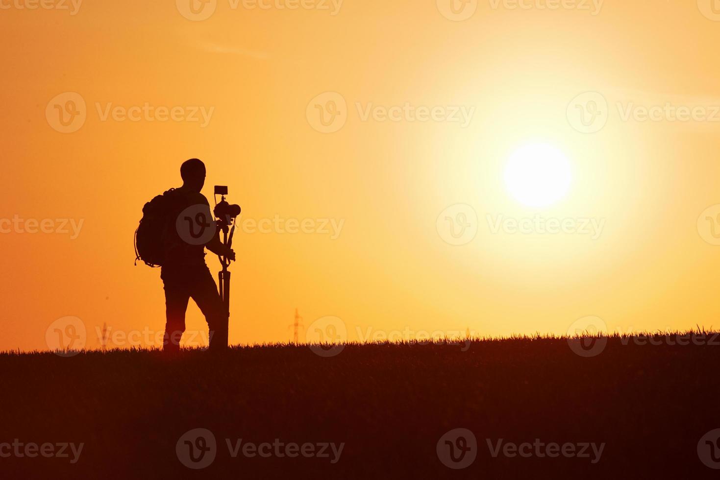 Photographer with professional equipments makes photos. Stands in the field illuminated by sunlight photo