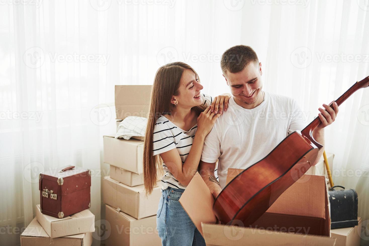 tiene guitarra acústica en las manos. pareja joven alegre en su nuevo apartamento. concepción de movimiento foto