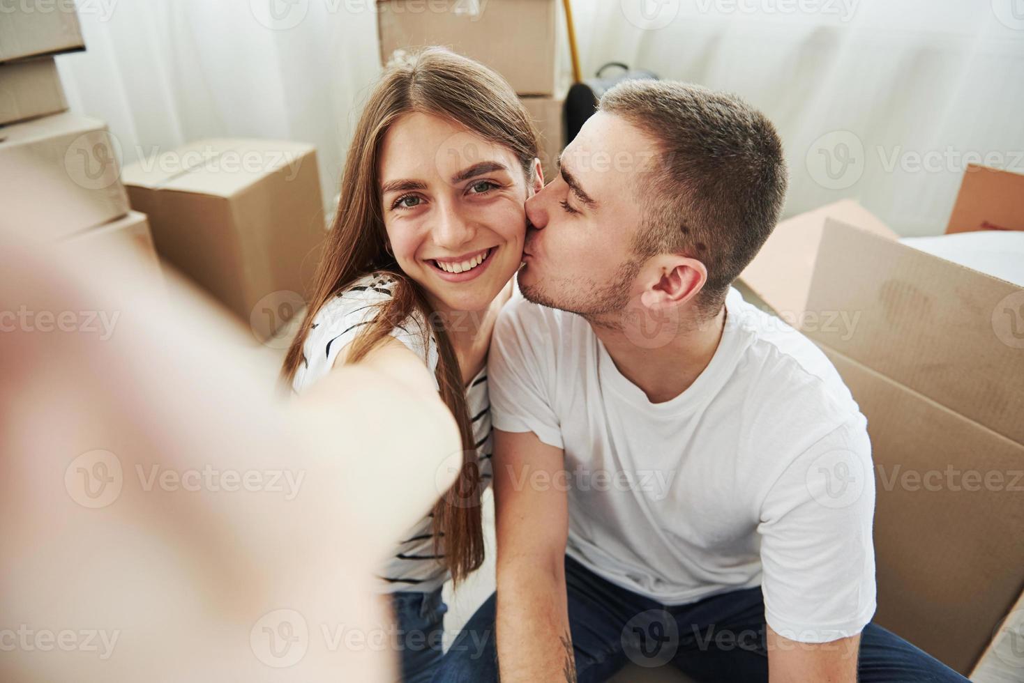 Making a photo. Guy kisses his wife. Cheerful young couple in their new apartment. Conception of moving photo