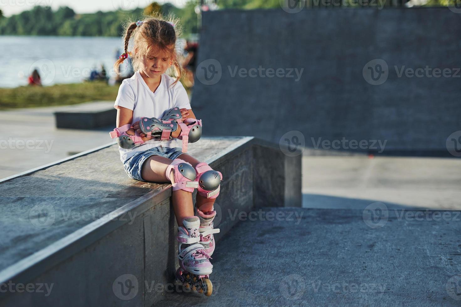 Cute little girl with roller skates outdoors sits on the ramp for extreme sports photo