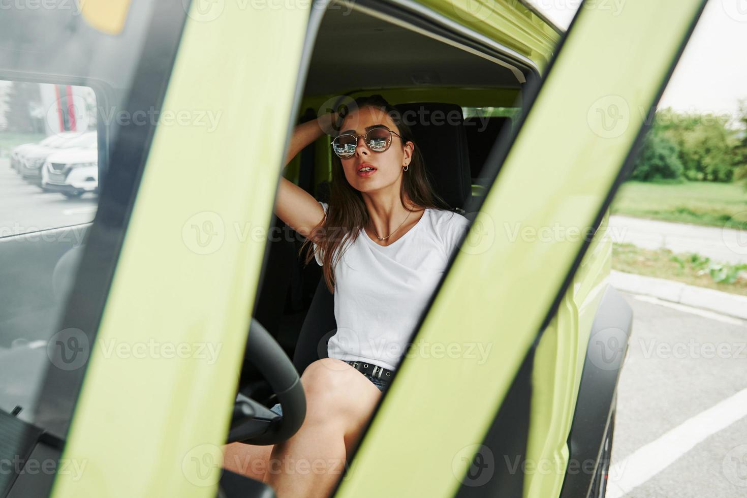 In sunglasses. Pretty woman in the green modern car posing for the camera photo