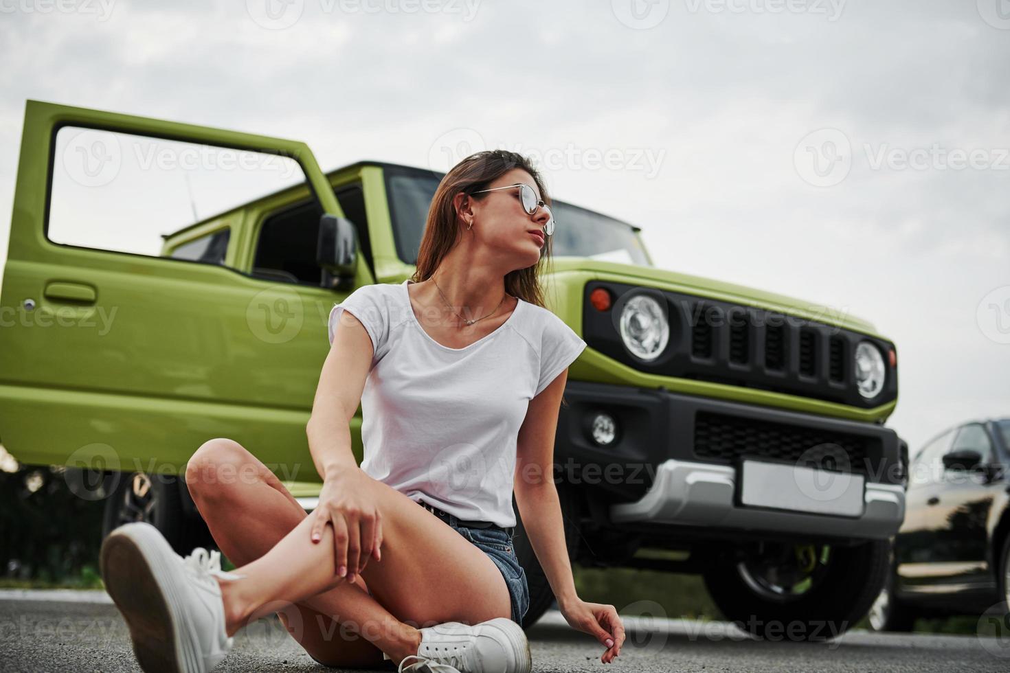 Sits and resting near new vehicle. Pretty woman in the green modern car posing for the camera photo