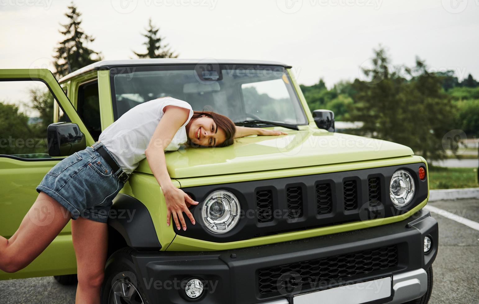 Stands near new vehicle. Pretty woman in the green modern car posing for the camera photo