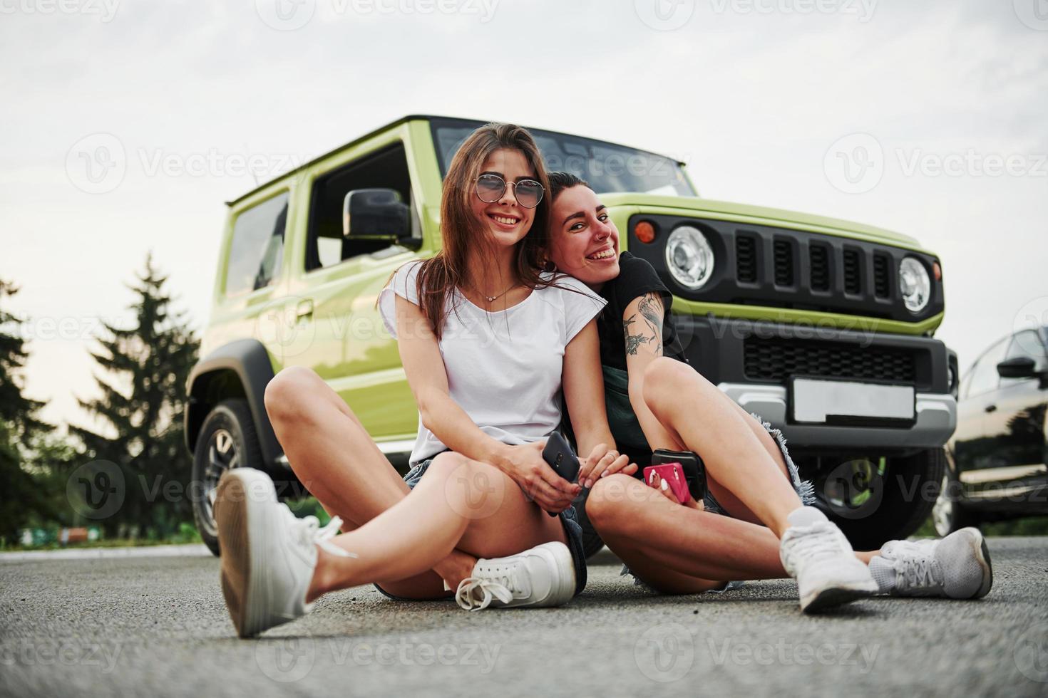 Two female friends have fun by sitting neat the new gren vehicle photo