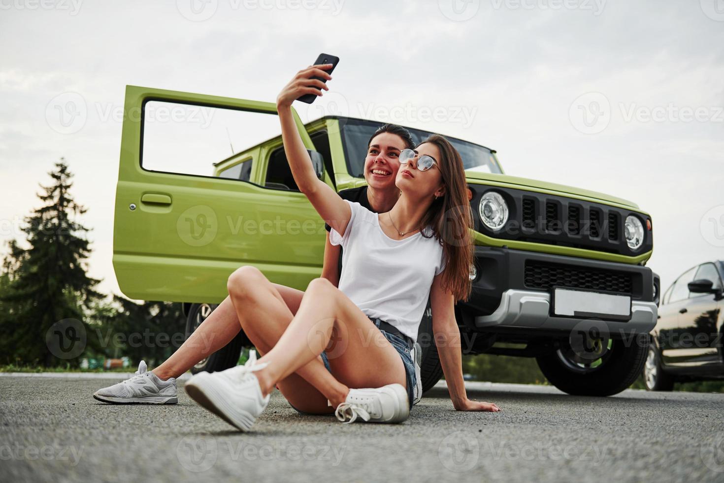 Two female friends have fun by sitting neat the new gren vehicle photo