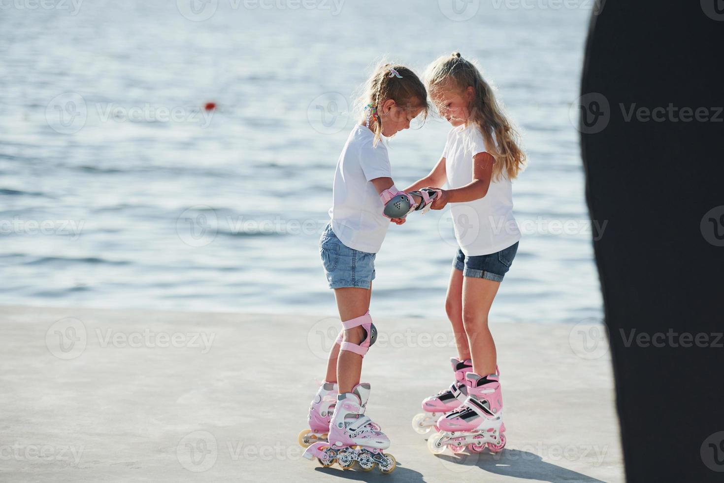 Two kids learning how to ride on roller skates at daytime near the lake photo