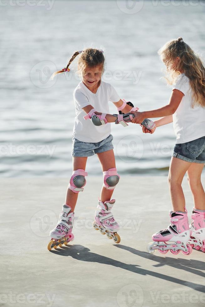 Two kids learning how to ride on roller skates at daytime near the lake