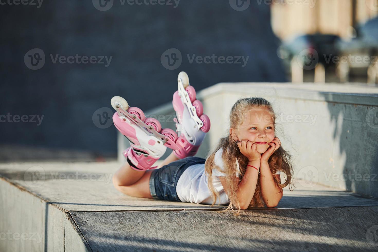 Cute little girl with roller skates outdoors sits on the ramp for extreme sports photo