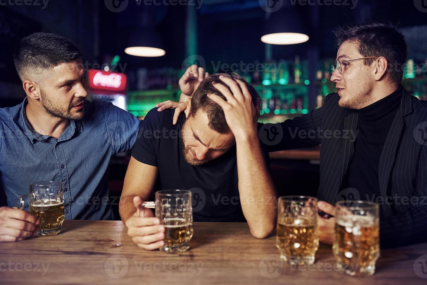 tres amigos varones en el bar. apoyando a un amigo triste. unidad de la gente. con cerveza en la mesa foto