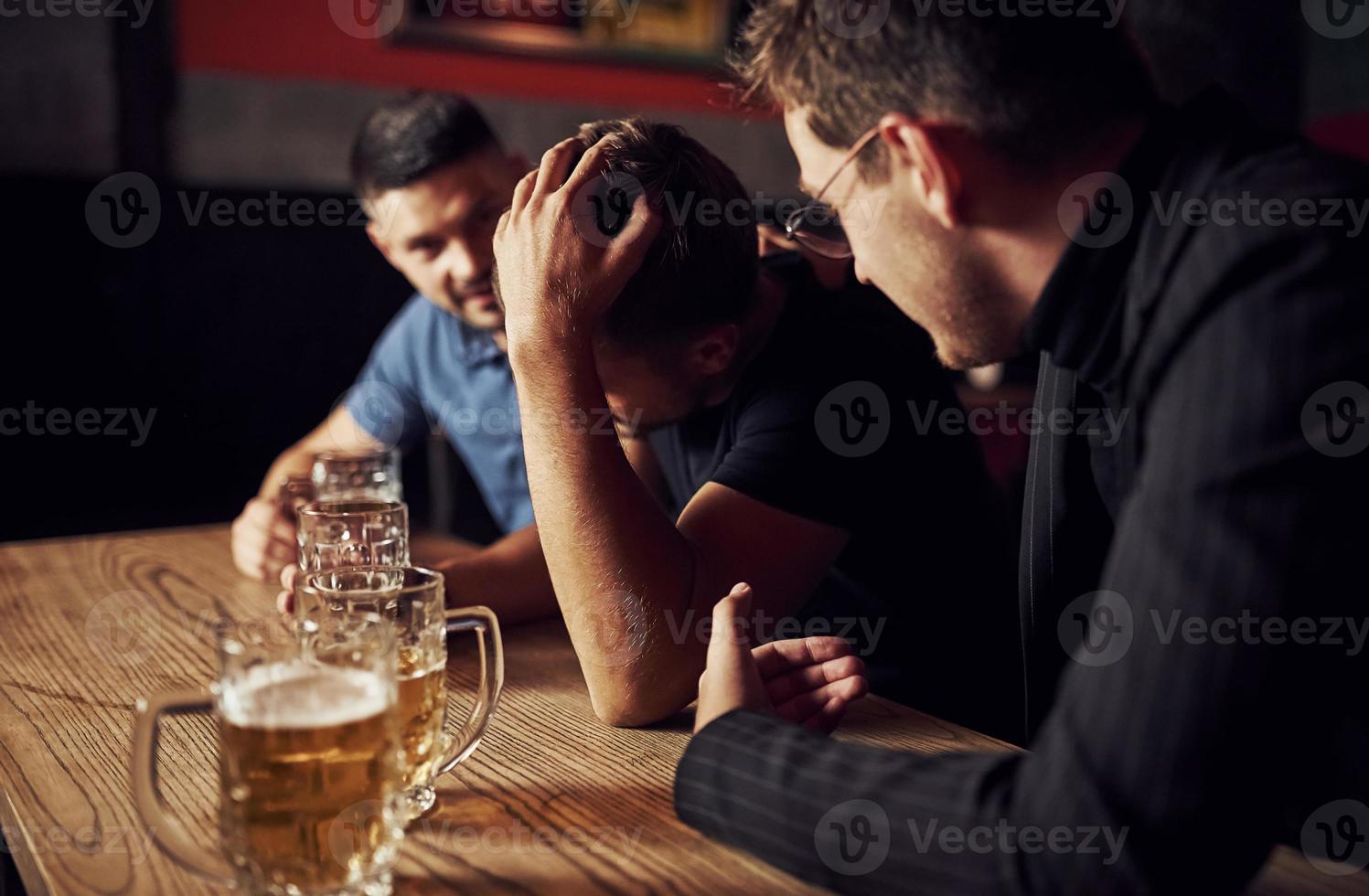 tres amigos varones en el bar. apoyando a un amigo triste. unidad de la gente. con cerveza en la mesa foto