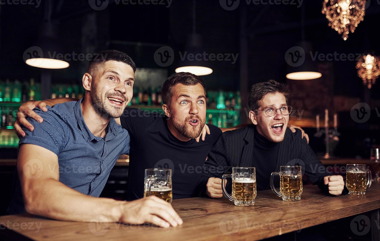 tres aficionados al deporte en un bar viendo fútbol. con cerveza en las manos foto