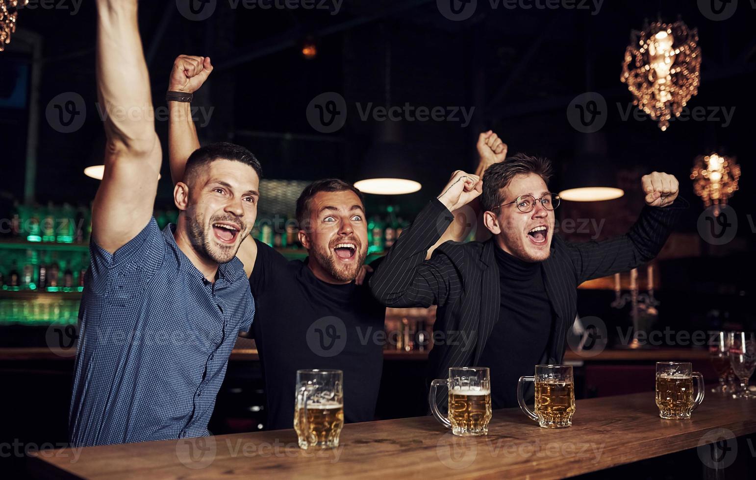 Celebrating victory. Three sports fans in a bar watching soccer. With beer in hands photo