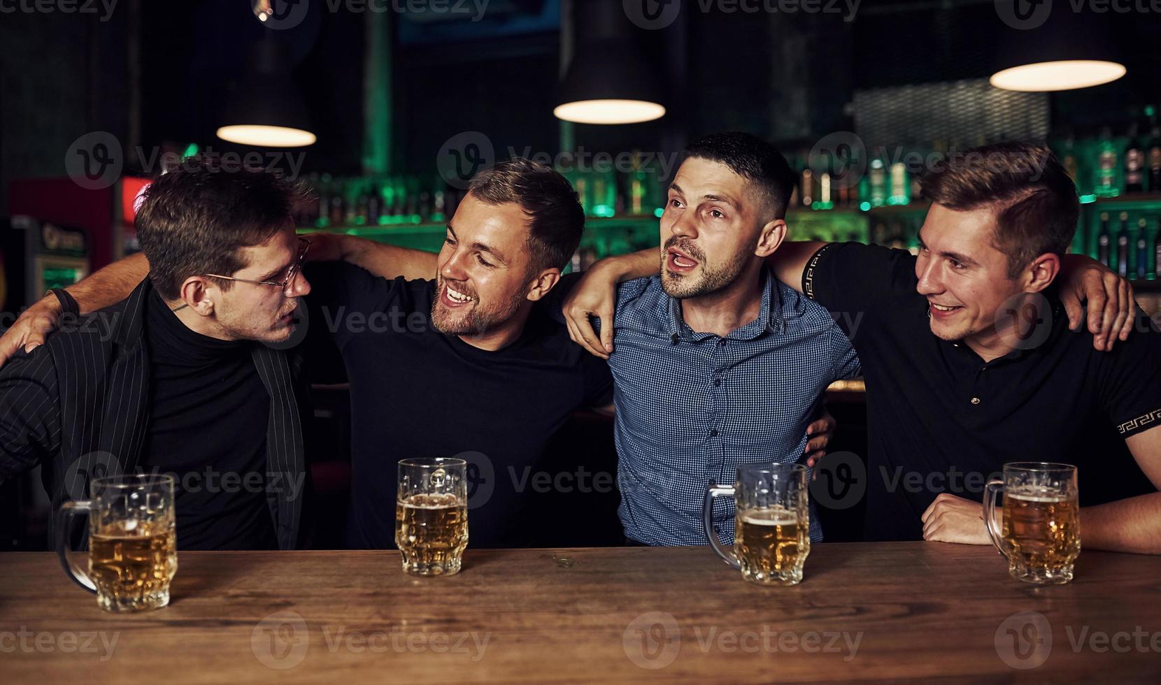 Three friends resting in the pub with beer in hands. Having conversation photo