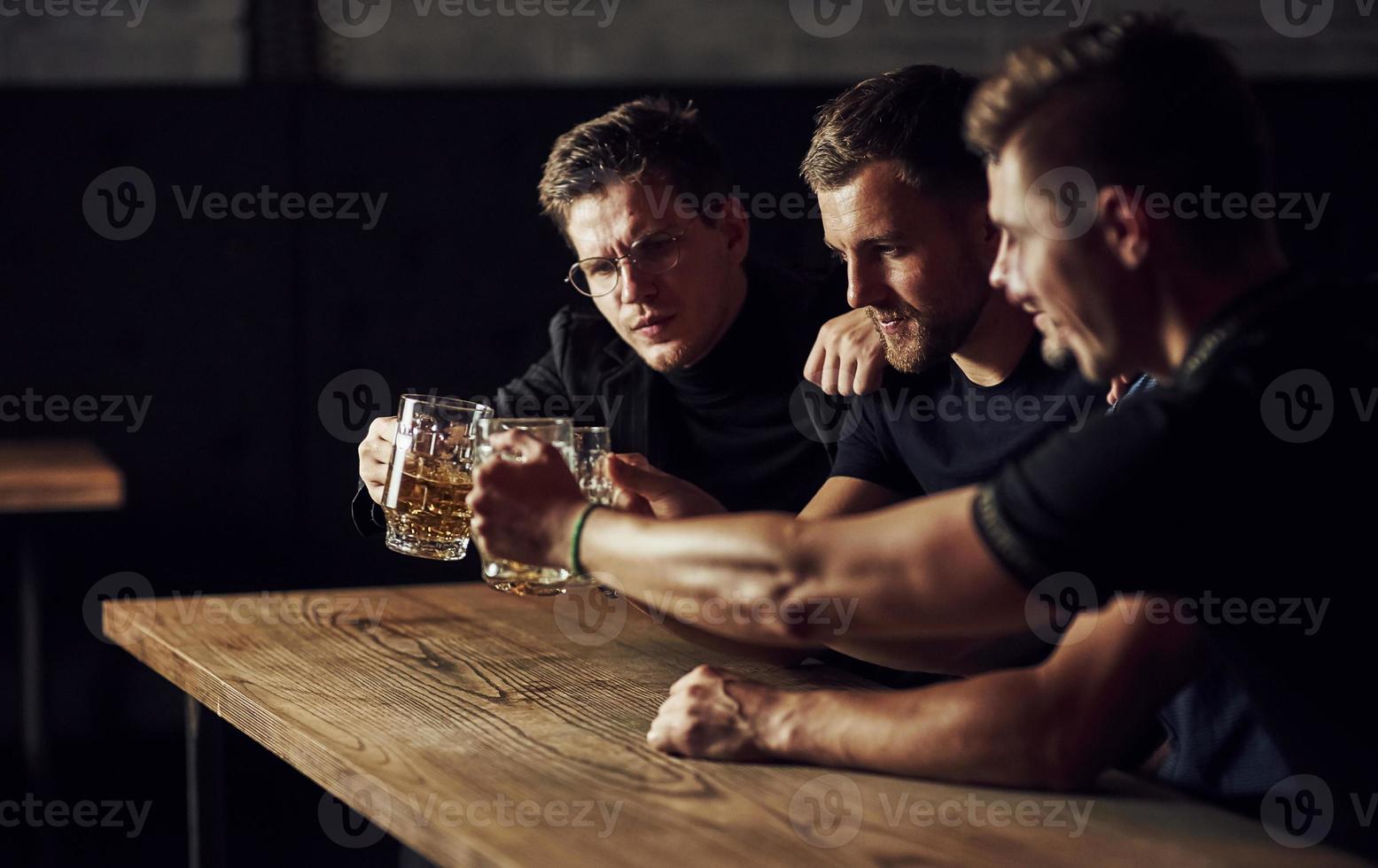 tres aficionados al deporte en un bar viendo fútbol. con cerveza en las manos foto