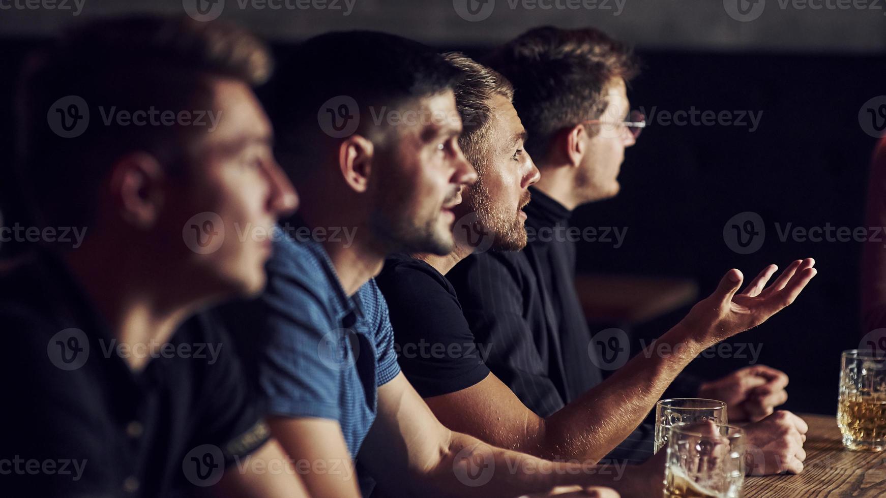 tres aficionados al deporte en un bar viendo fútbol. con cerveza en las manos foto