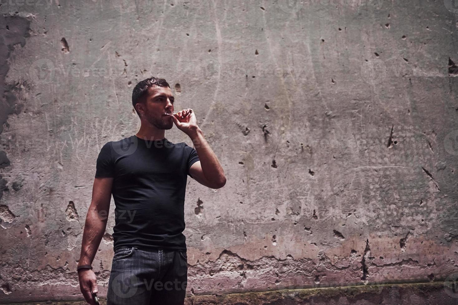 Portrait of man in black shirt smoking on the background of old cracked wall photo