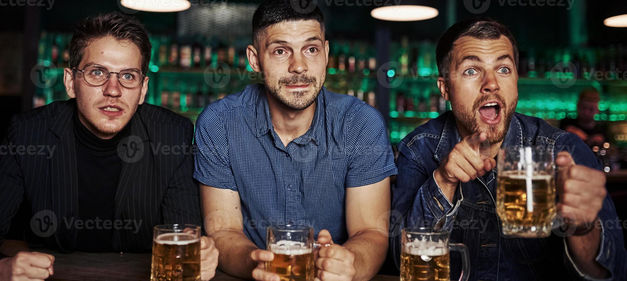 Sincere emotions. Three sports fans in a bar watching soccer. With beer in hands photo