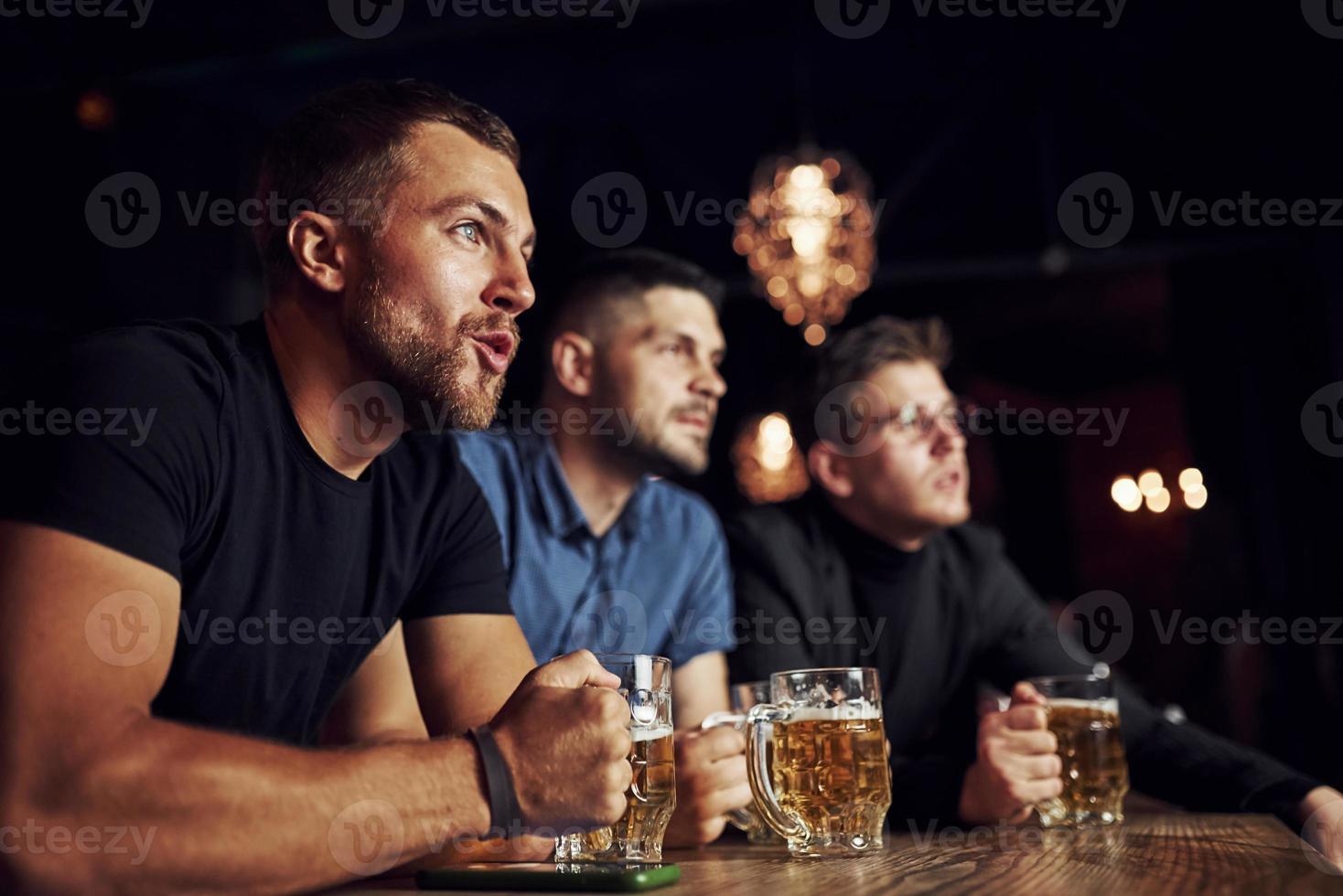 tres aficionados al deporte en un bar viendo fútbol. con cerveza en las manos foto