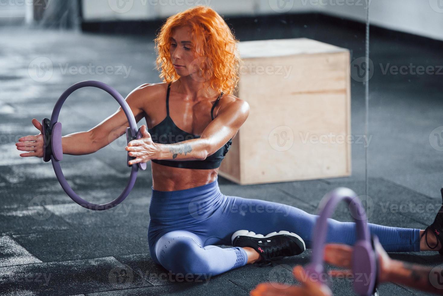 With special equipment. Sporty redhead girl have fitness day in gym at daytime. Muscular body type photo