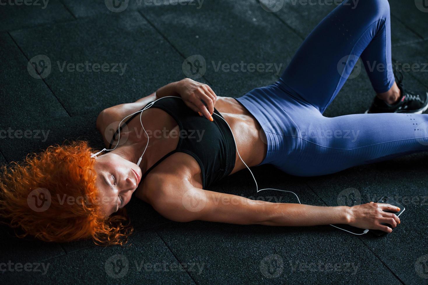 Tired, lying down. Sporty redhead girl have fitness day in gym at daytime. Muscular body type photo