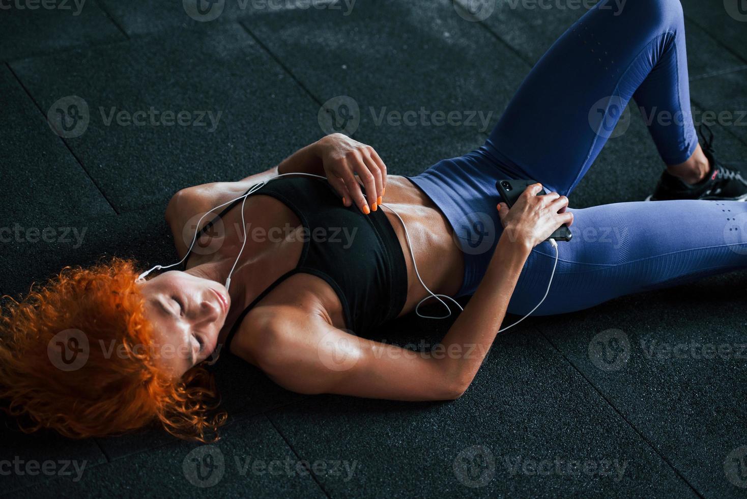 Tired, lying down. Sporty redhead girl have fitness day in gym at daytime. Muscular body type photo