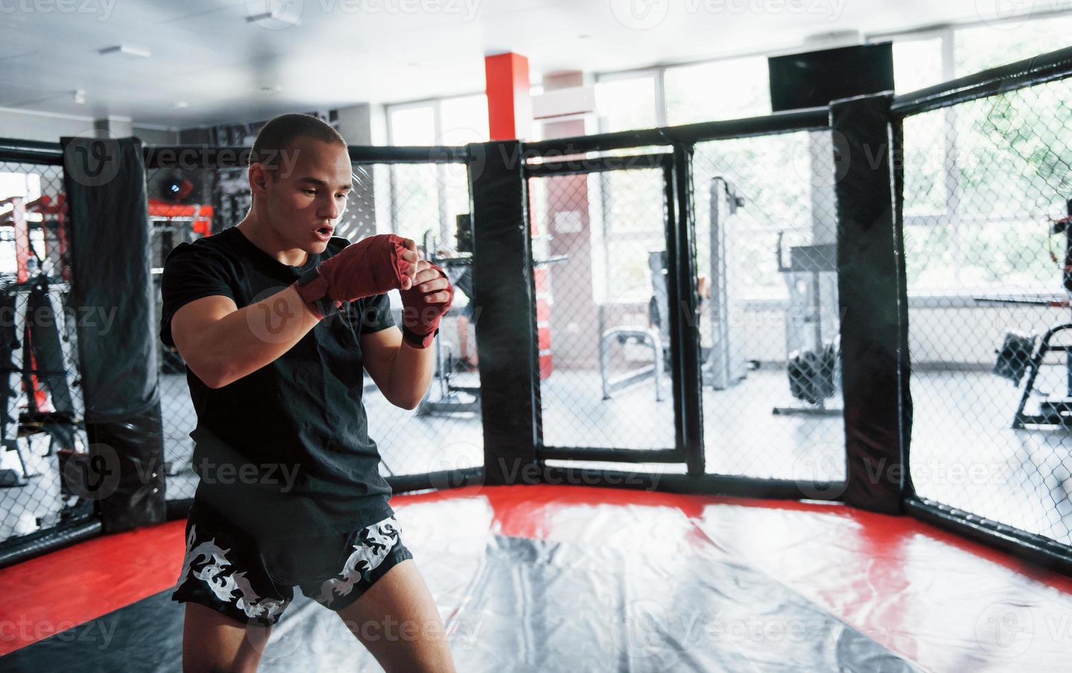 Young boxer in red bandages have exercise. In the gym on the cage photo