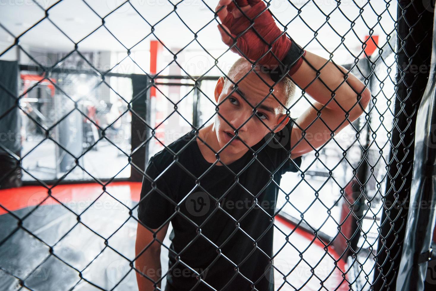 tomando un descanso. deportista en el ring de boxeo tiene ejercicio. apoyado en la cerca foto