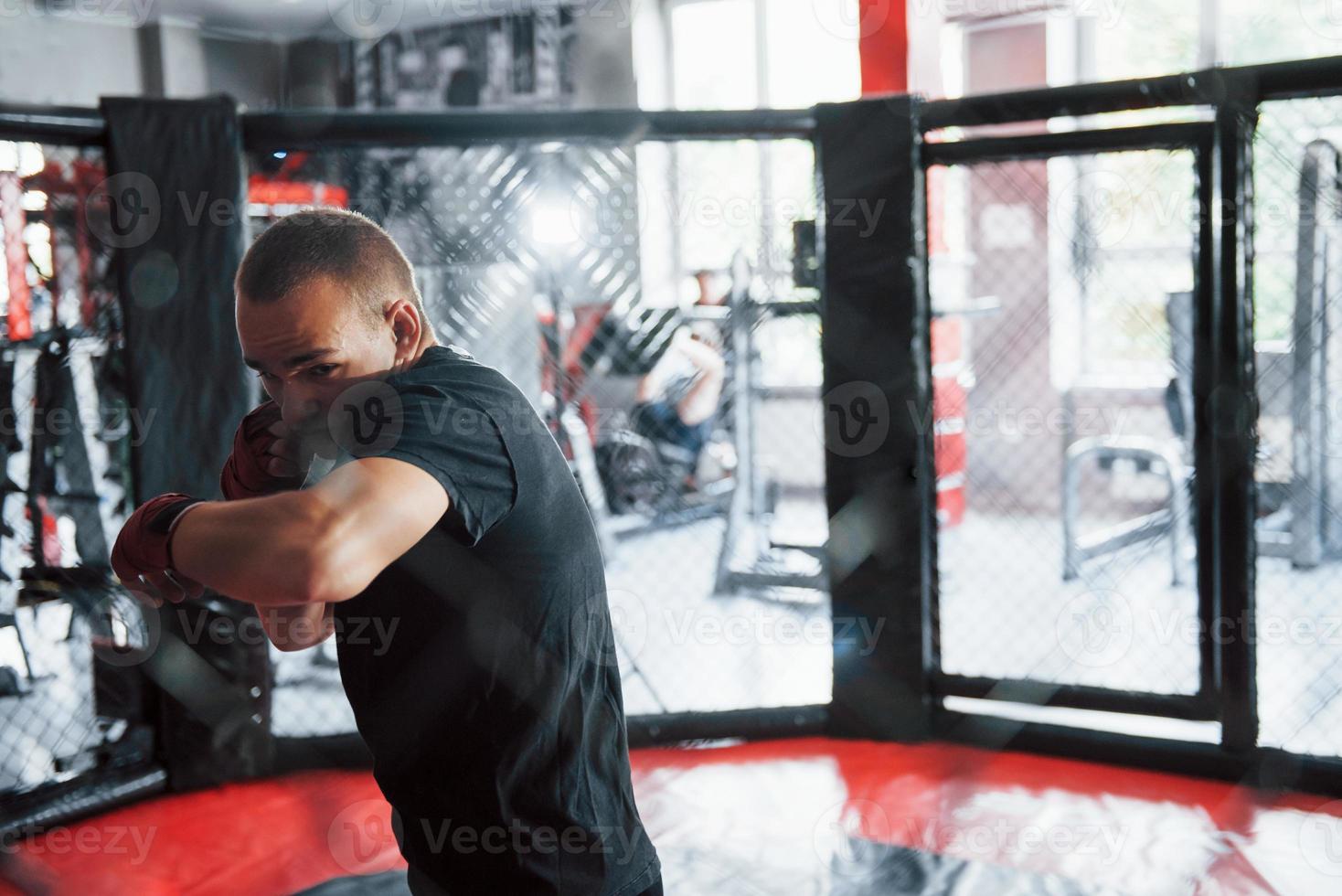 Front view. Young boxer in red bandages have exercise. In the gym on the cage photo