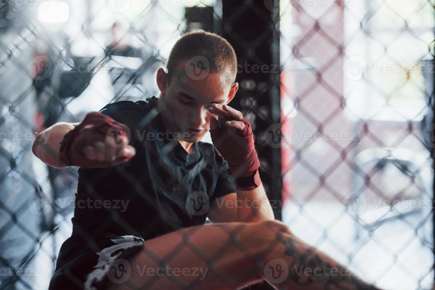 Front view. Young boxer in red bandages have exercise. In the gym on the cage photo