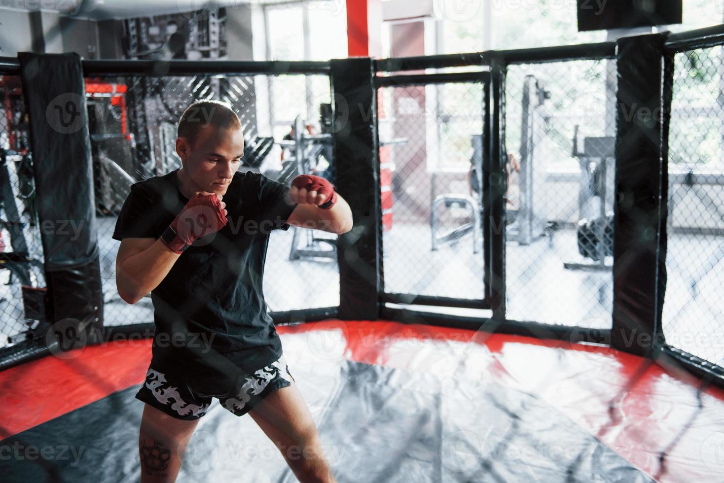 Young boxer in red bandages have exercise. In the gym on the cage photo