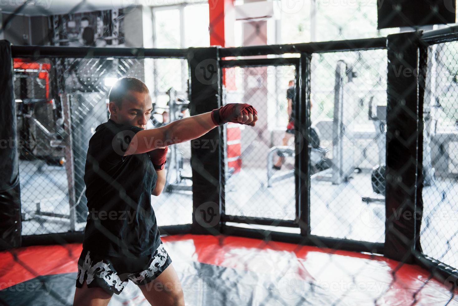 Young boxer in red bandages have exercise. In the gym on the cage photo