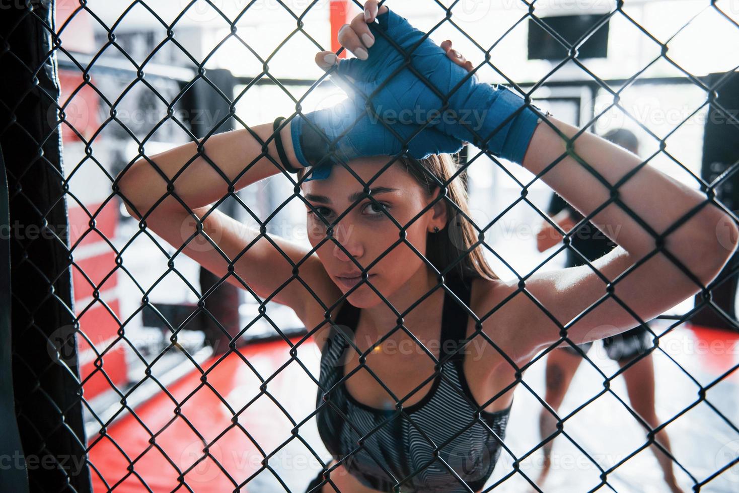 tomando un descanso. la deportista en el ring de boxeo tiene ejercicio. apoyado en la cerca foto