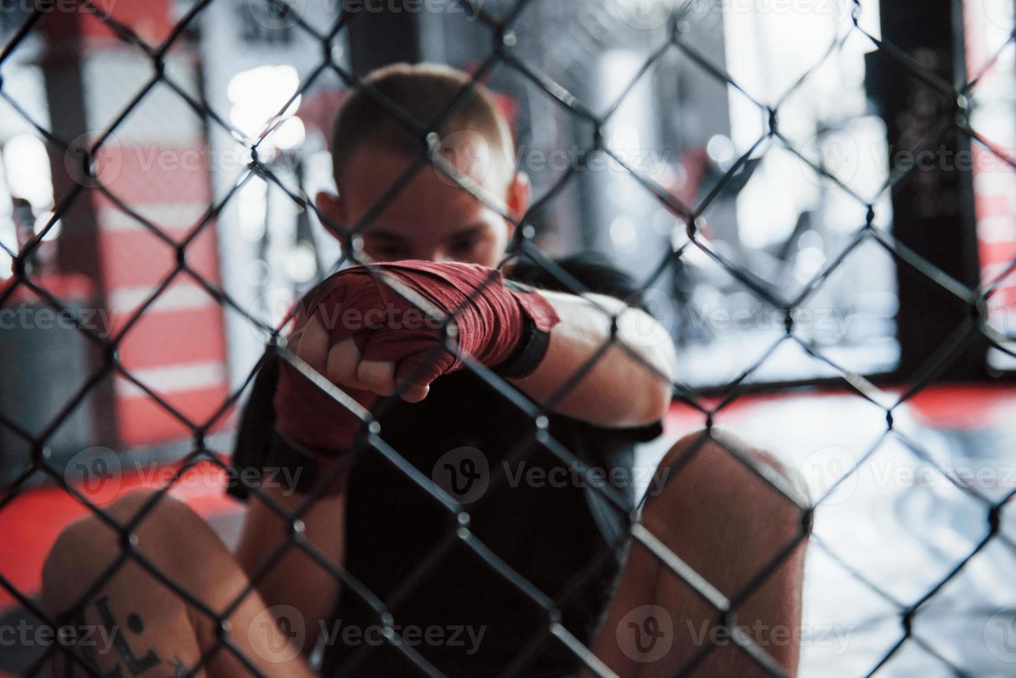 From down position. Young boxer in red bandages have exercise. In the gym on the cage photo