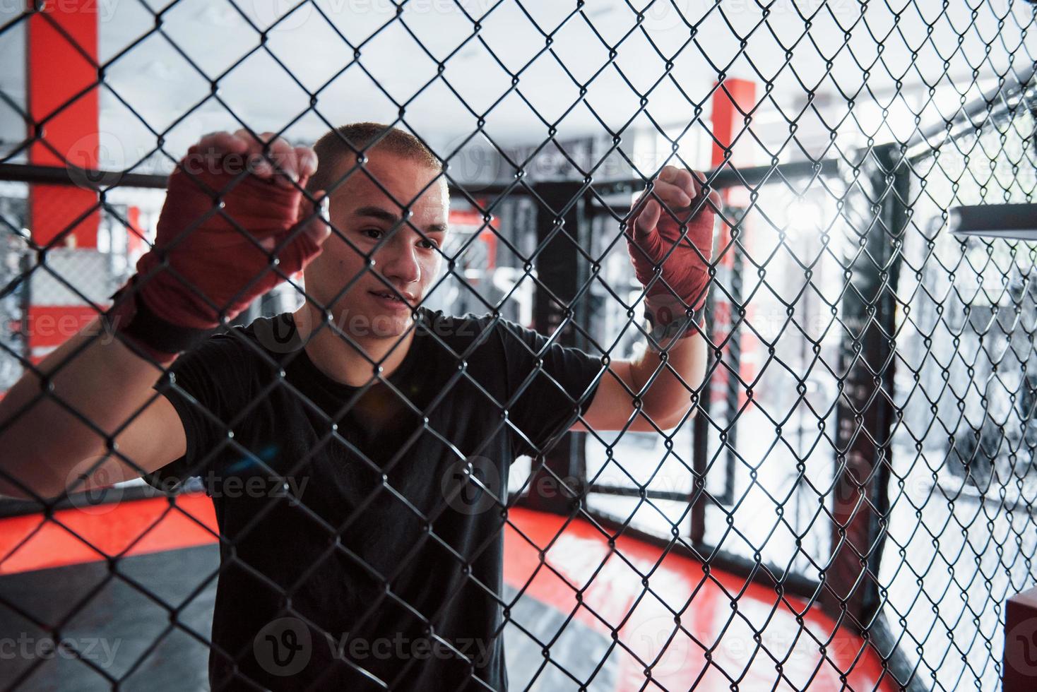 tomando un descanso. deportista en el ring de boxeo tiene ejercicio. apoyado en la cerca foto