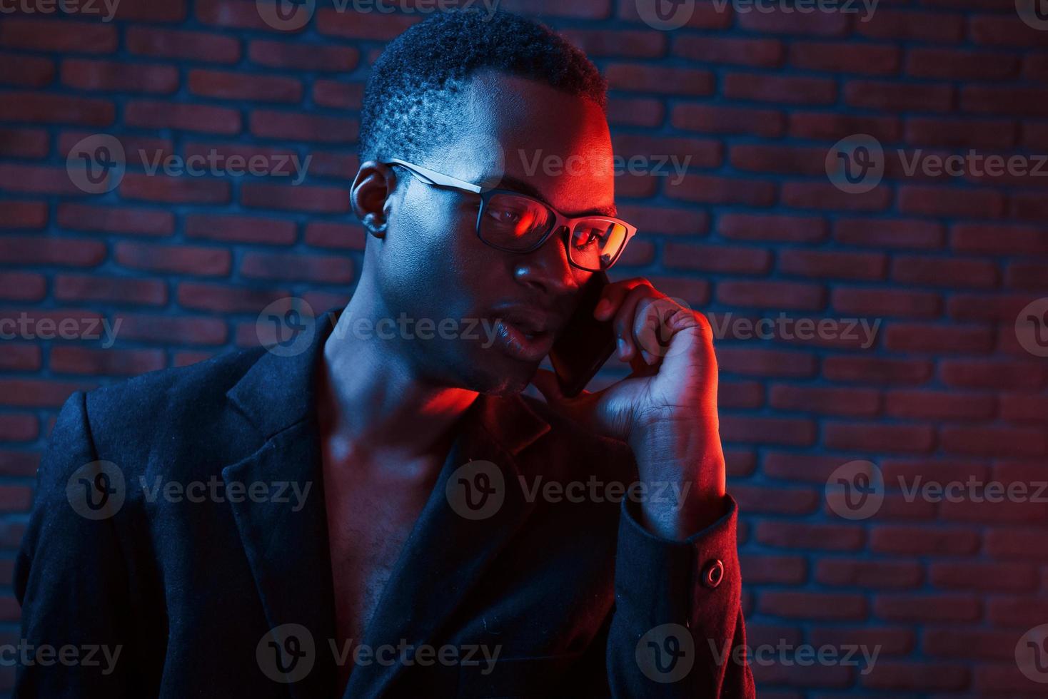 Having conversation by using phone. Futuristic neon lighting. Young african american man in the studio photo