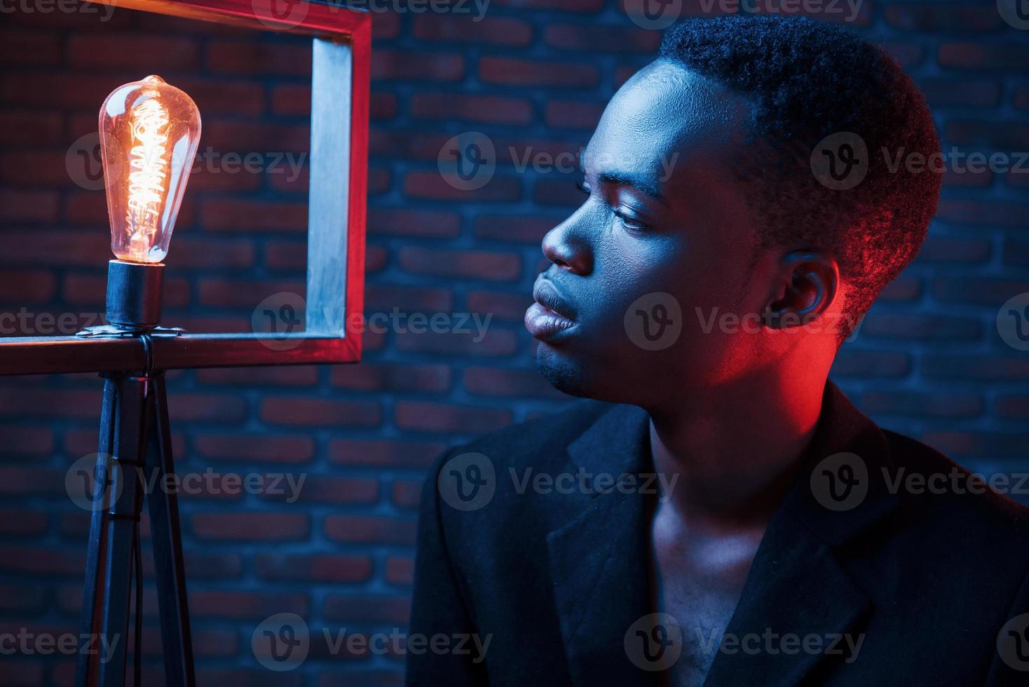 Looks at bulb. Futuristic neon lighting. Young african american man in the studio photo