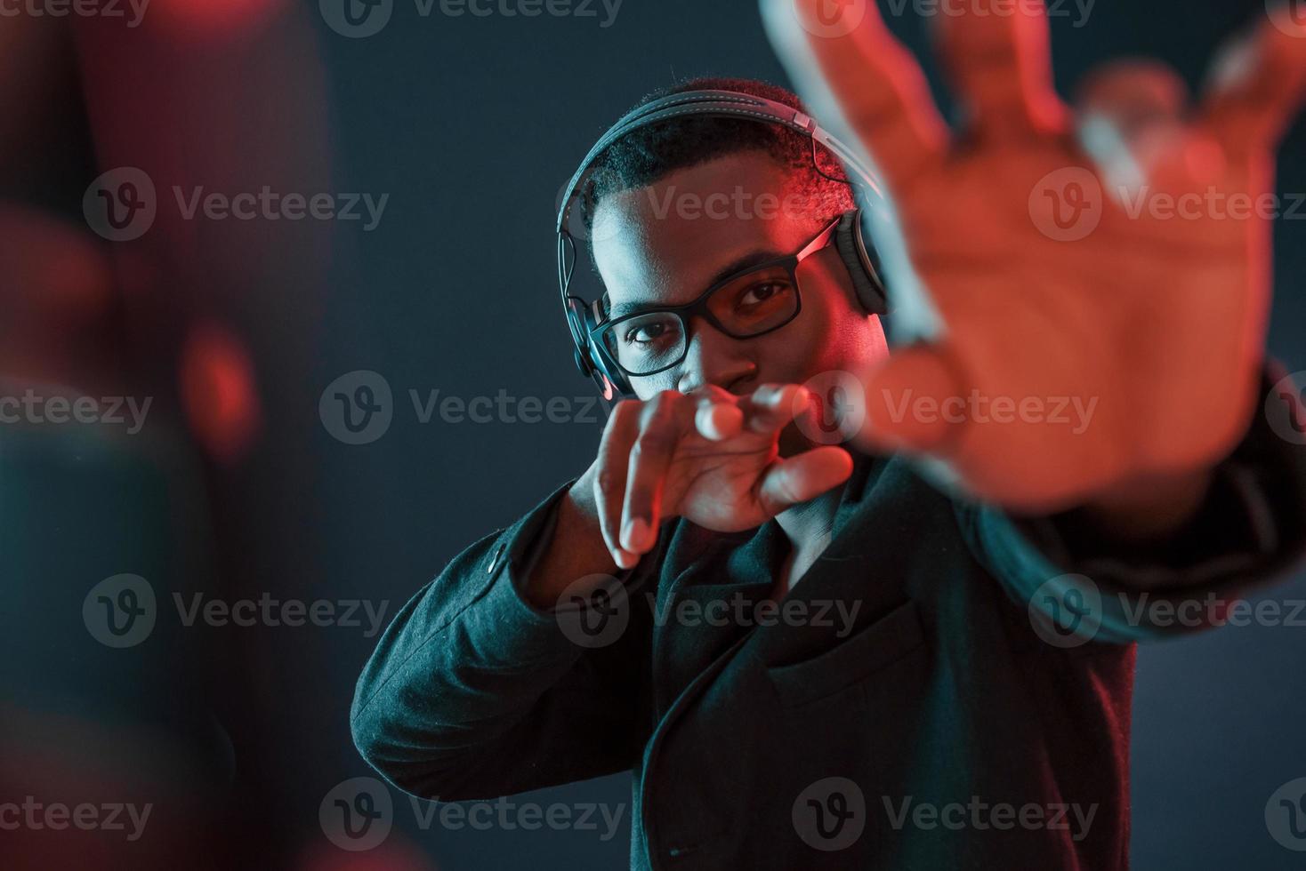 Enjoying listening music in headphones. In glasses. Futuristic neon lighting. Young african american man in the studio photo