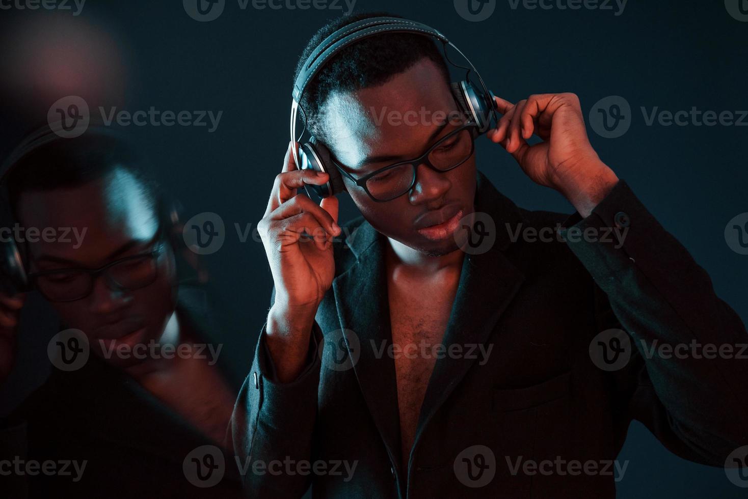 disfrutando escuchando música en auriculares. en vasos iluminación de neón futurista. joven afroamericano en el estudio foto