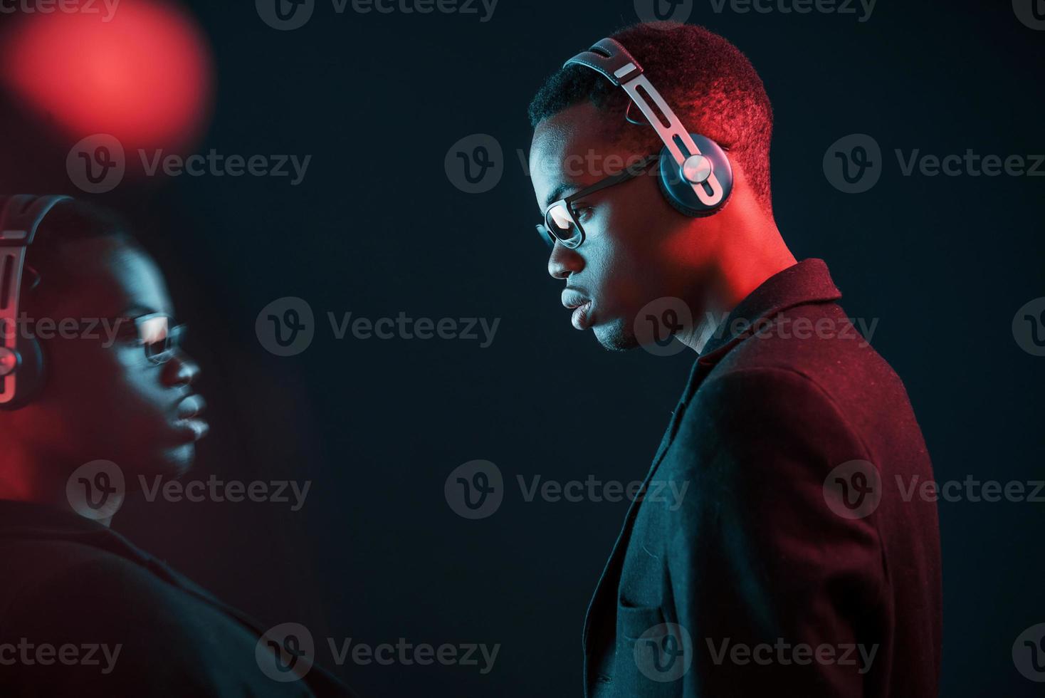 Enjoying listening music in headphones. In glasses. Futuristic neon lighting. Young african american man in the studio photo