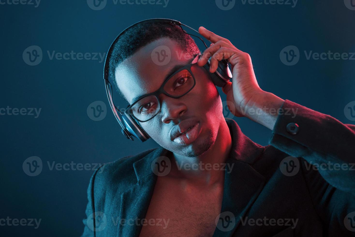 Enjoying listening music in headphones. In glasses. Futuristic neon lighting. Young african american man in the studio photo