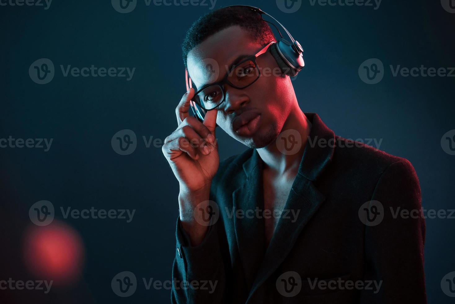 Enjoying listening music in headphones. In glasses. Futuristic neon lighting. Young african american man in the studio photo